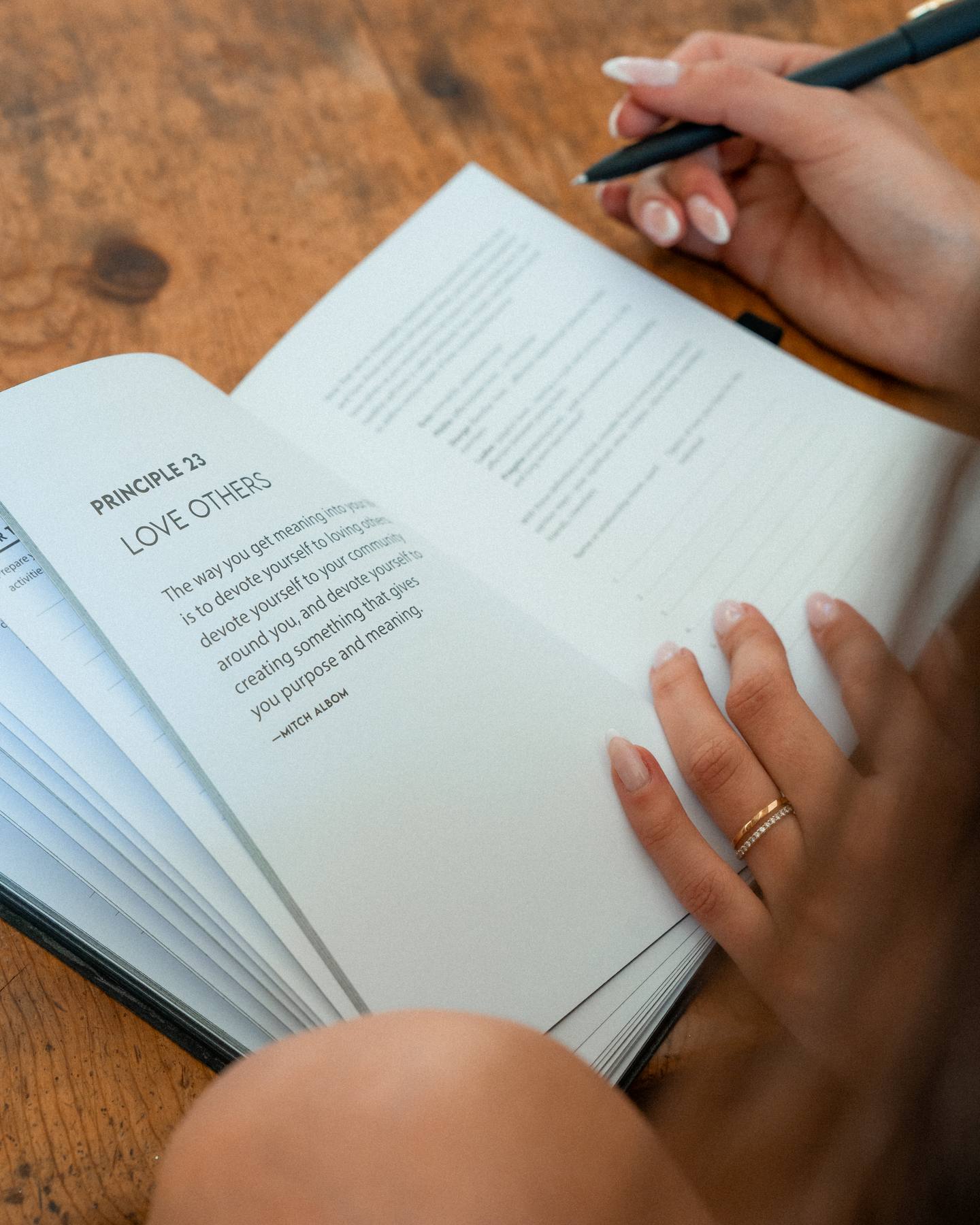 Writing in The Epic Journal's Principle 23 page, pen in hand at a wooden table